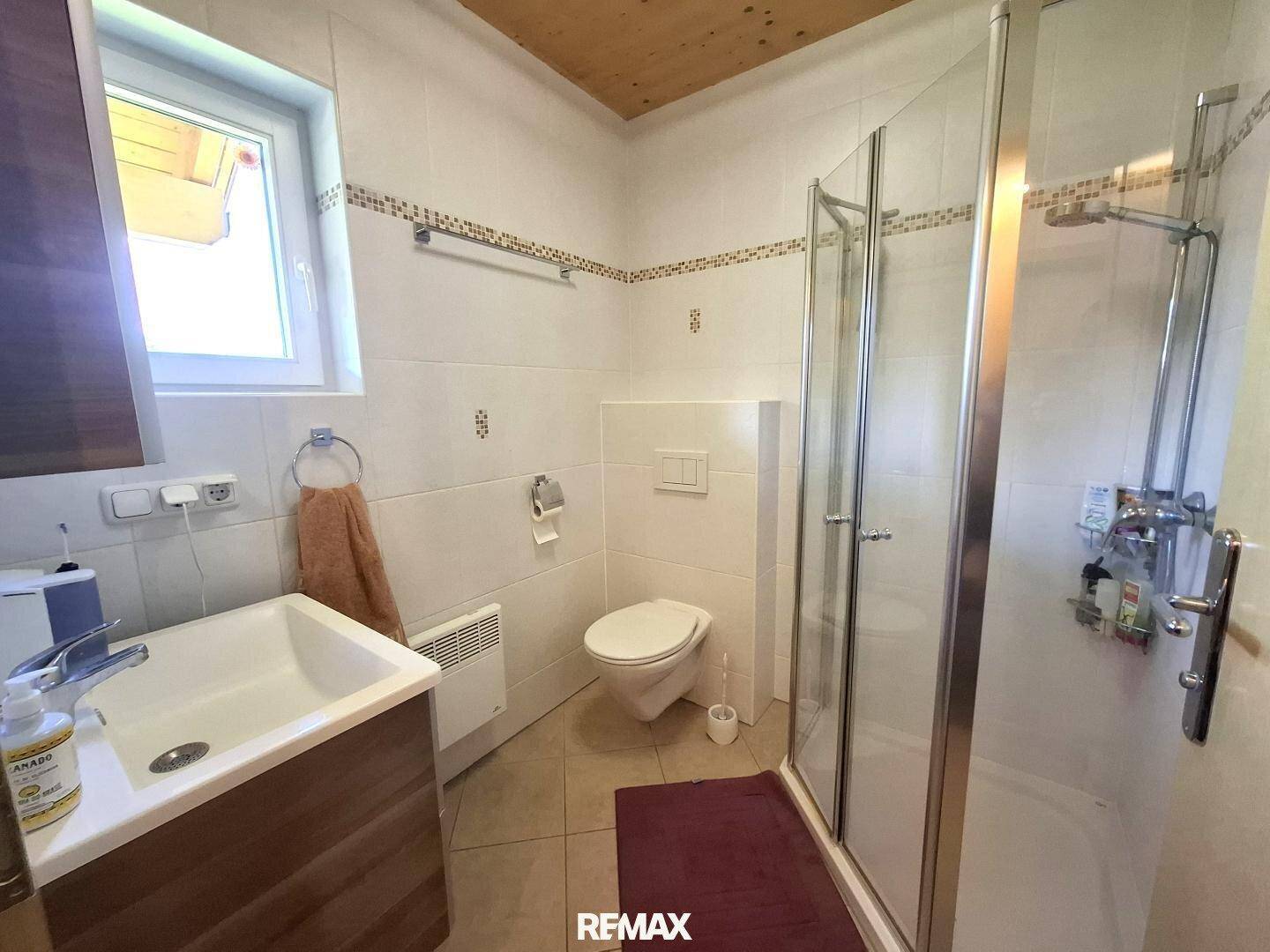 Badezimmer mit Dusche, WC, Waschbecken und Fenster für Tageslicht.