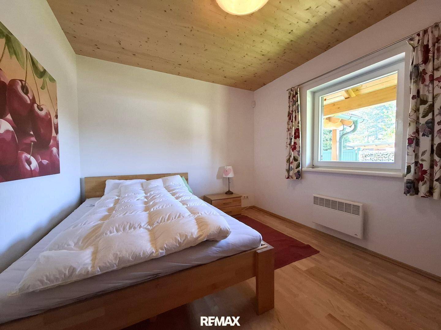 Schlafzimmer mit Holzbett, Holzbalkendecke und Fenster mit Blick ins Grüne.