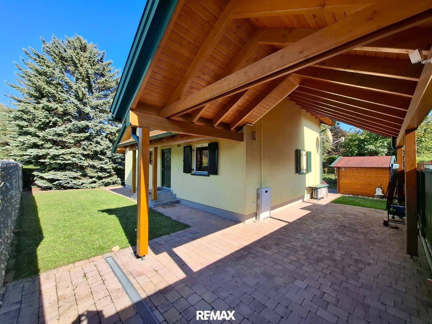 Überdachter Carport-Bereich mit Holzdach und gepflasterter Einfahrt.