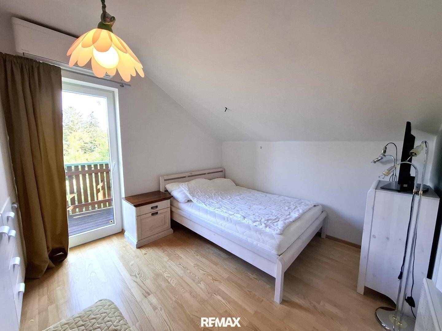 Helles Schlafzimmer im Dachgeschoss mit Holzboden und Balkonzugang.