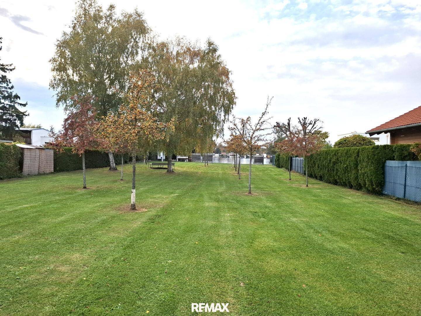 Großer Garten mit Rasenfläche, Bäumen und direktem Zugang zum Wasser.