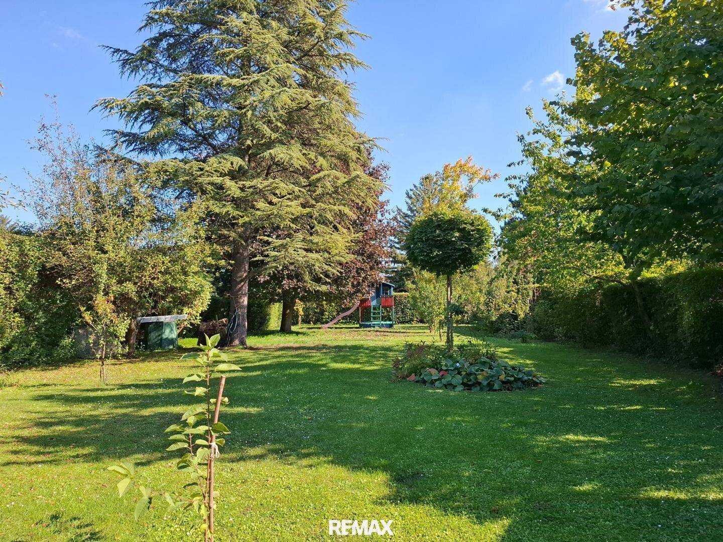 Weitläufiger Garten mit Rasenfläche, Bäumen und Spielgeräten im Hintergrund.