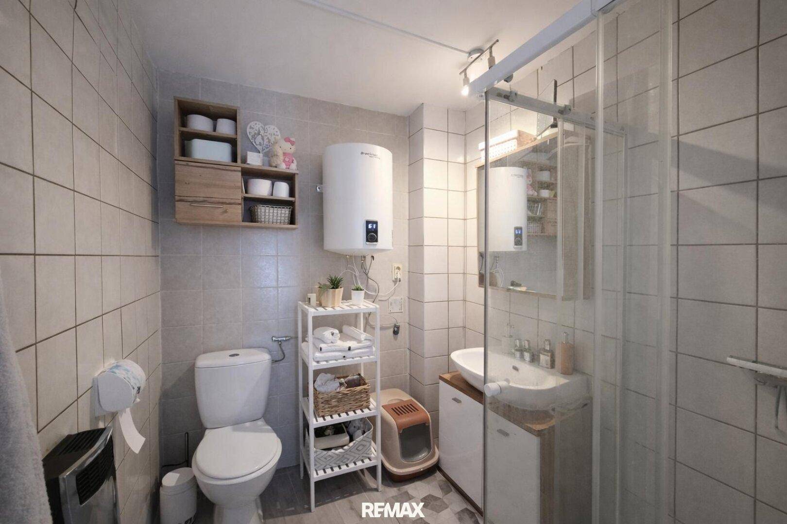 Badezimmer mit Duschkabine, Toilette, Waschbecken und hellgrauen Fliesen an den Wänden.