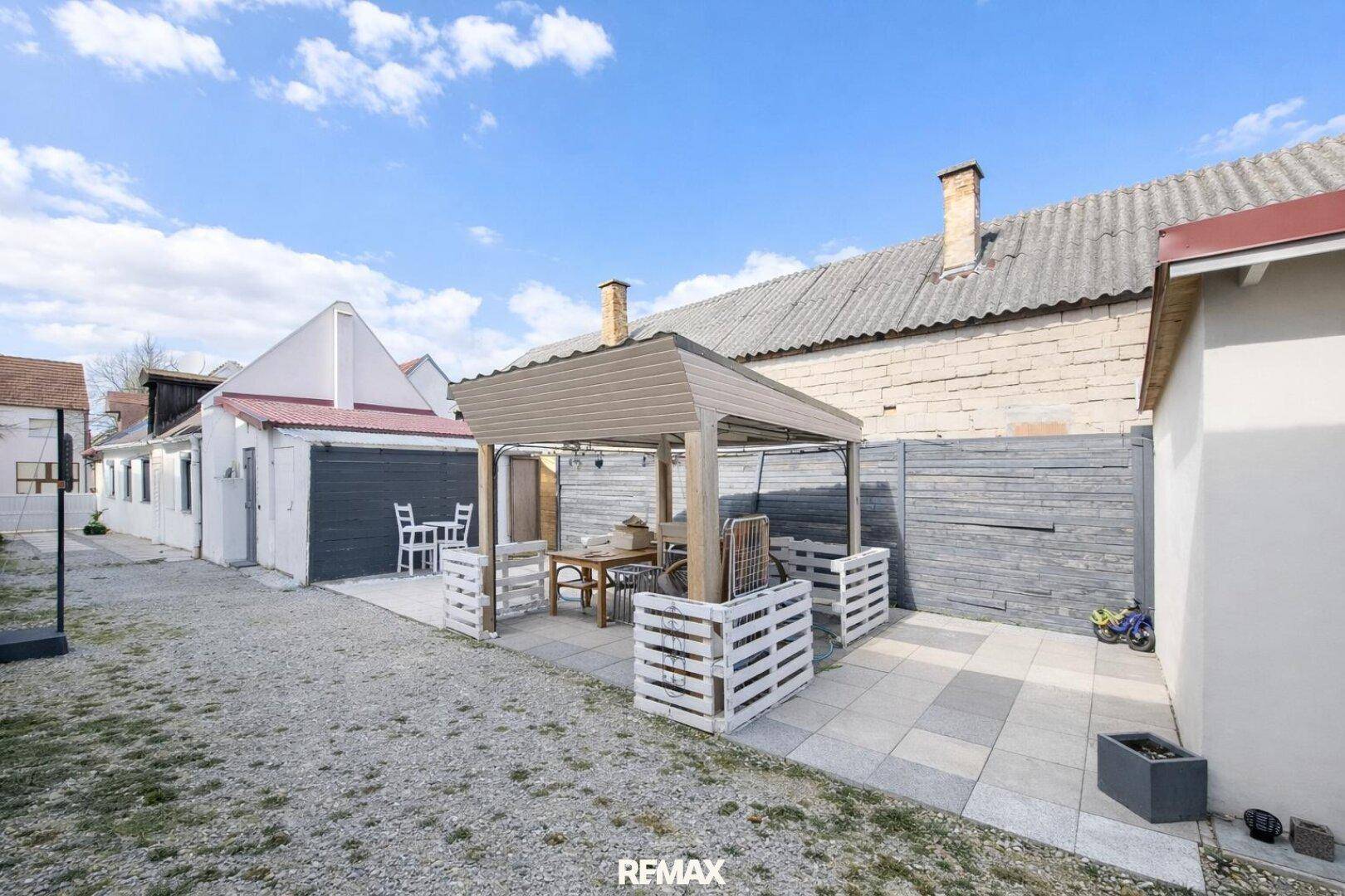 Gemütlicher Außenbereich mit Pergola, Esstisch und Stühlen auf einem Kiesgrundstück.