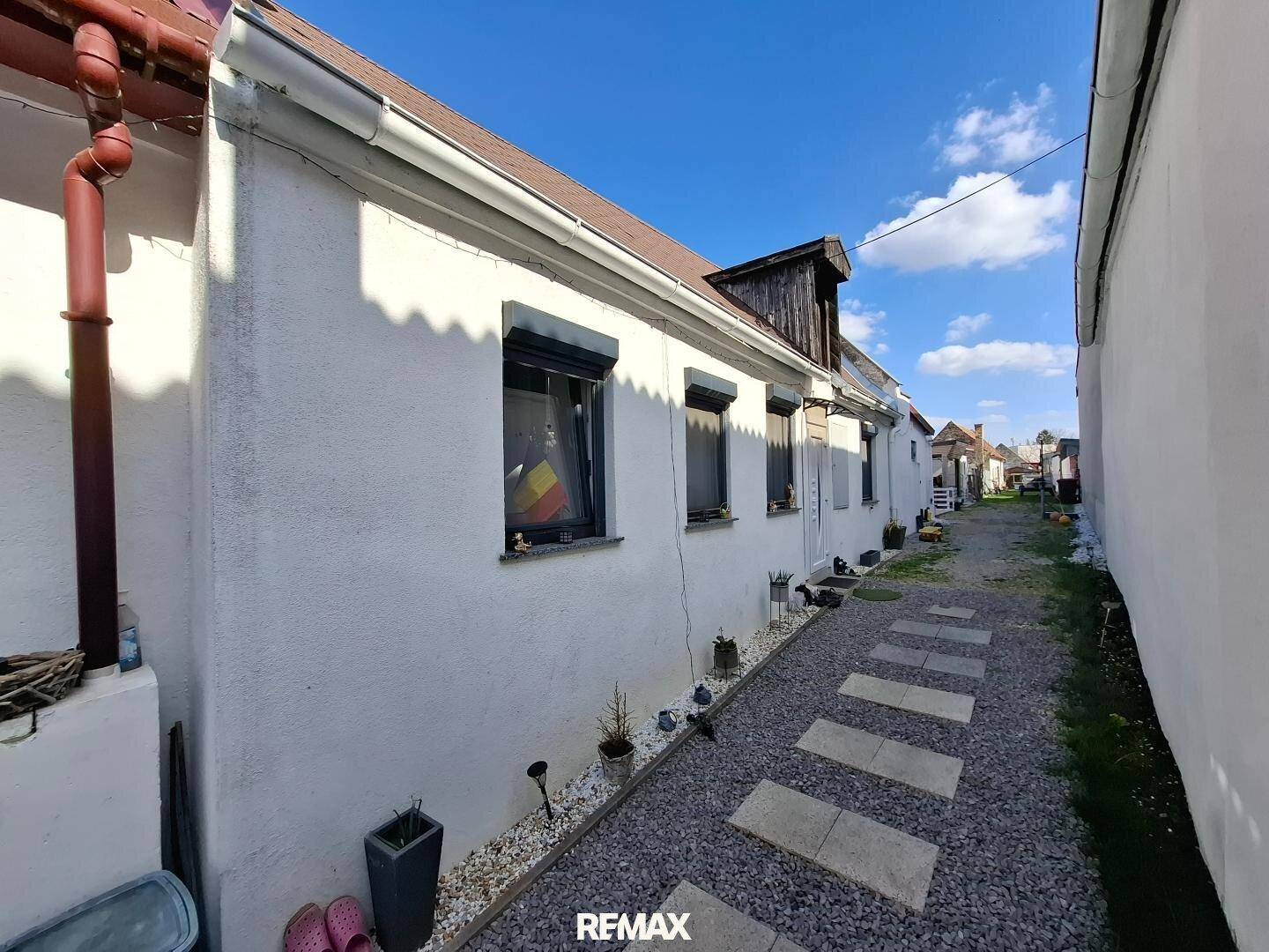Seitenansicht des weißen Hauses mit schmalem Kiesweg und kleinen Pflanzen entlang der Fassade.