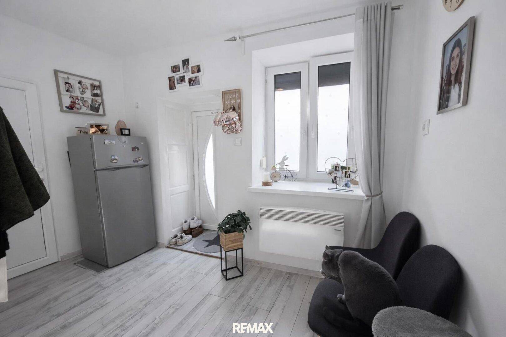 Heller Eingangsbereich mit Kühlschrank, Fenster und Sitzgelegenheiten, ideal für den Empfang.
