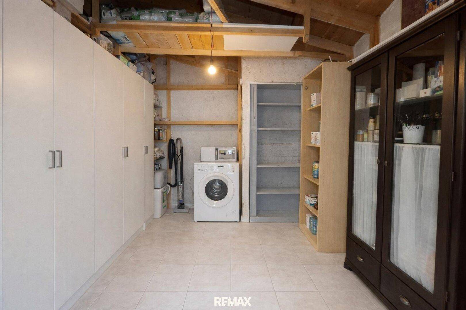 Hauswirtschaftsraum mit Waschmaschine, Regalen und Schränken unter sichtbaren Holzbalken.