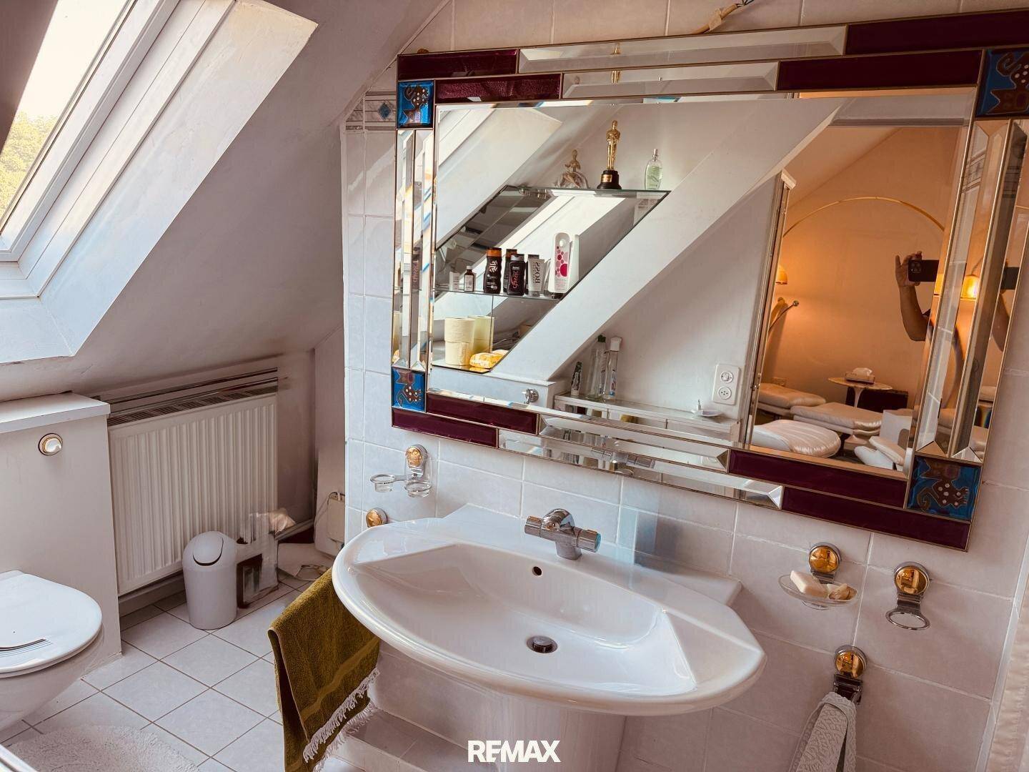 Badezimmer im Dachgeschoss mit Waschbecken, Spiegel, WC und Dachfenster.