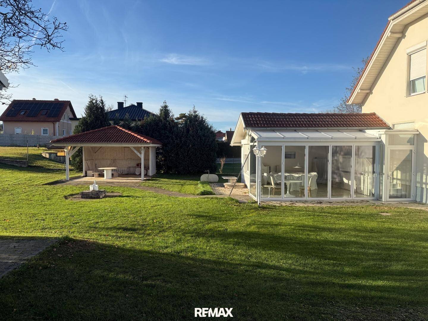 Großer Garten mit Wintergarten, Gartenlaube und viel Grünfläche.