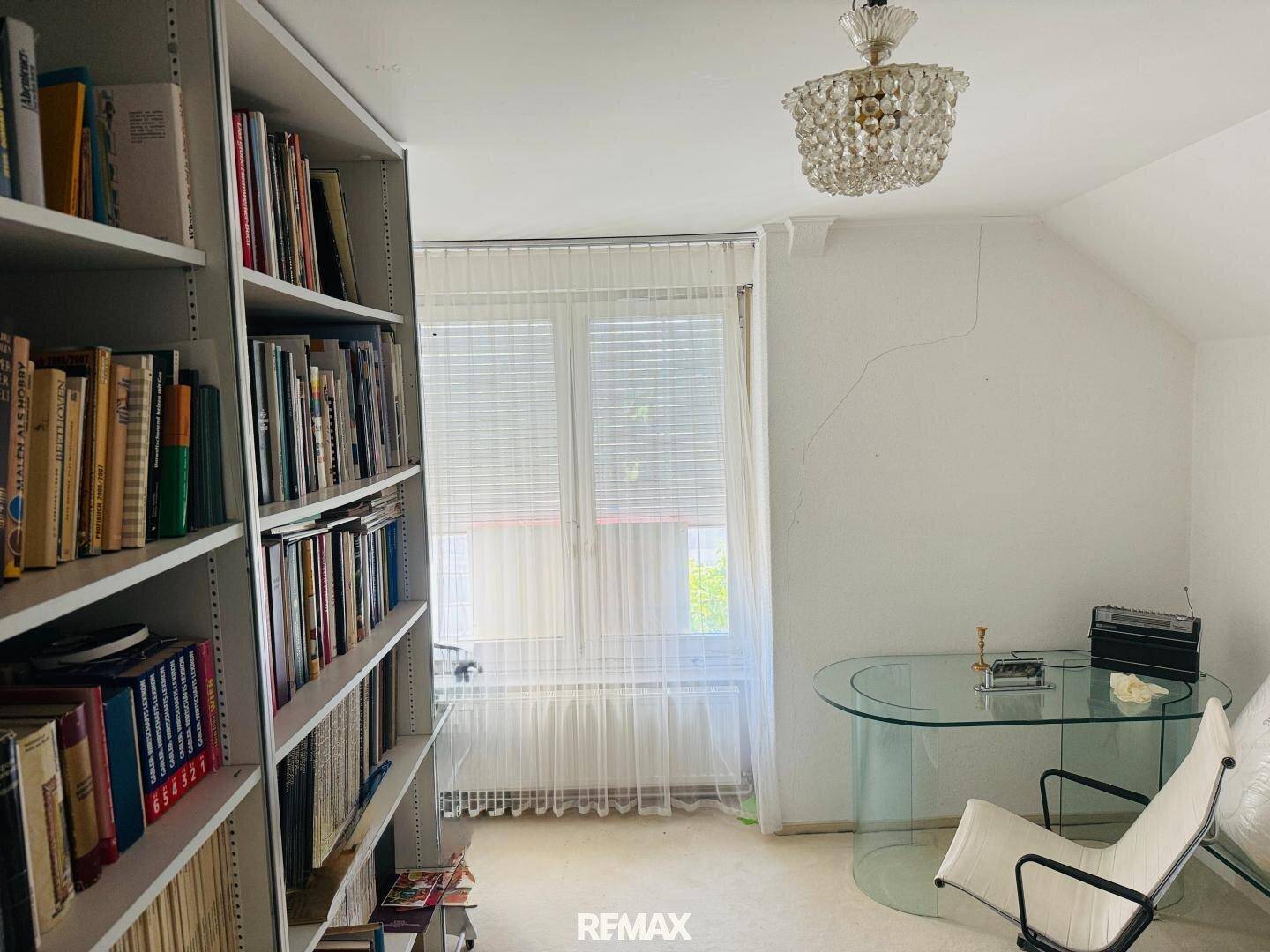 Helles Arbeitszimmer im Dachgeschoss mit Bücherregalen, Glas-Schreibtisch und Dachschräge.