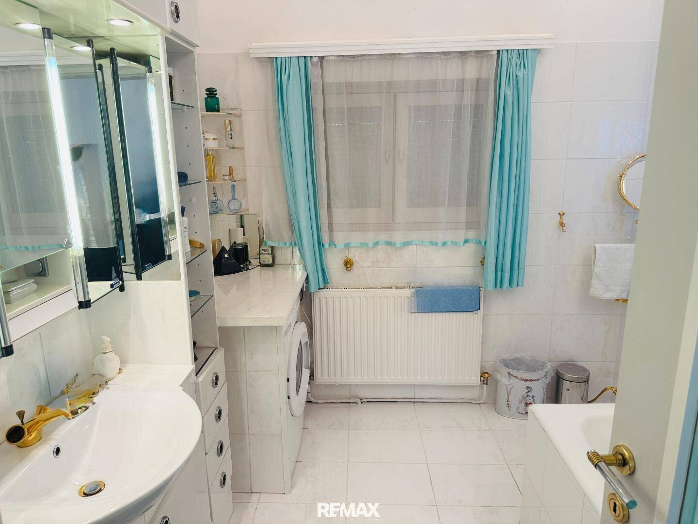 Helles Badezimmer mit Waschbecken, Waschmaschine und Fenster, dekoriert in Türkis.