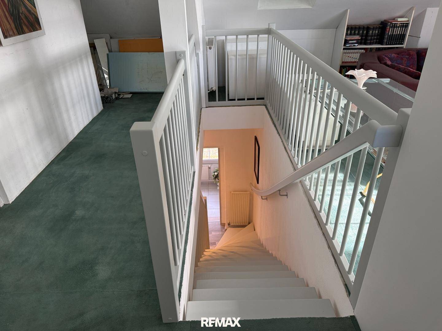 Treppenhaus mit weiß gestrichener Holztreppe und grünem Teppichboden.