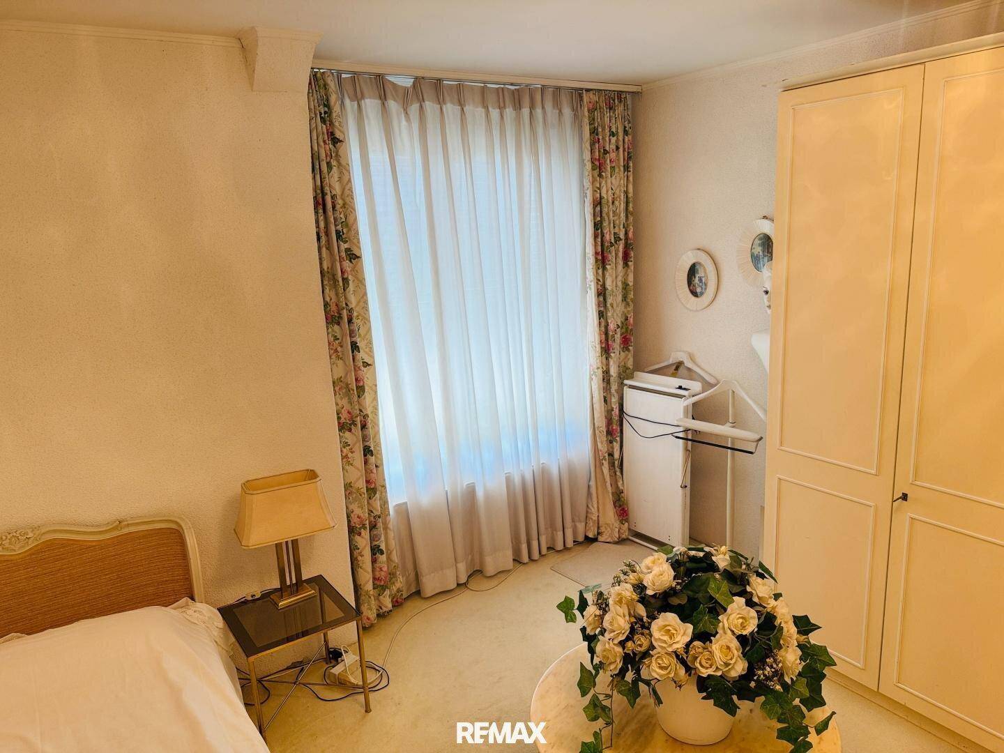 Gemütliches Schlafzimmer mit floralen Vorhängen, Teppichboden und Einbauschrank.