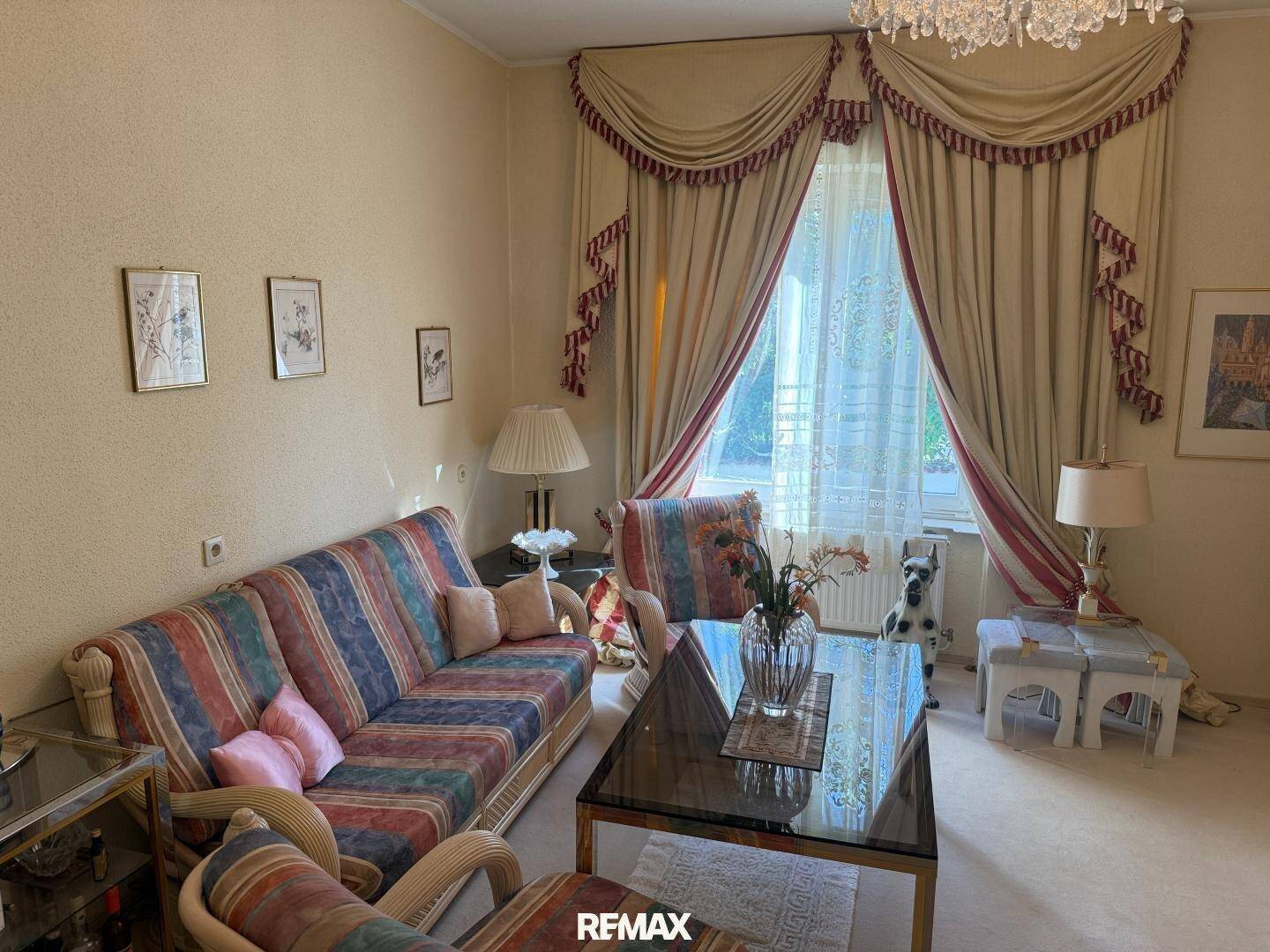 Gemütliches Wohnzimmer mit gestreiftem Sofa, Teppichboden und schweren Vorhängen.