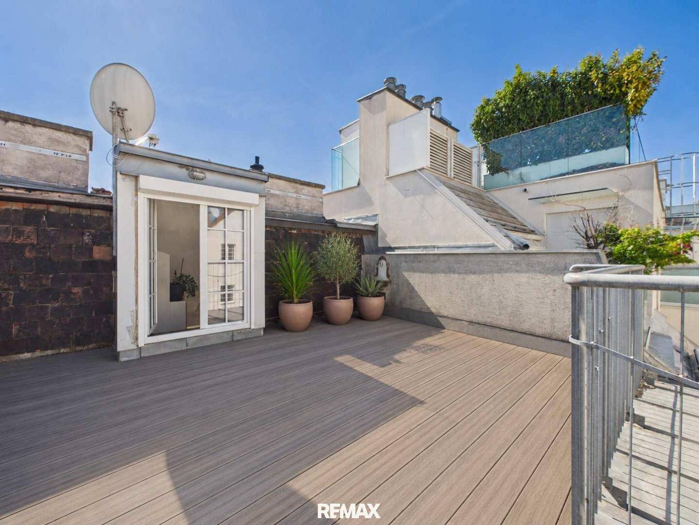 Weitläufige Dachterrasse mit Holzdeck, Pflanzen und Blick auf die umliegenden Gebäude.