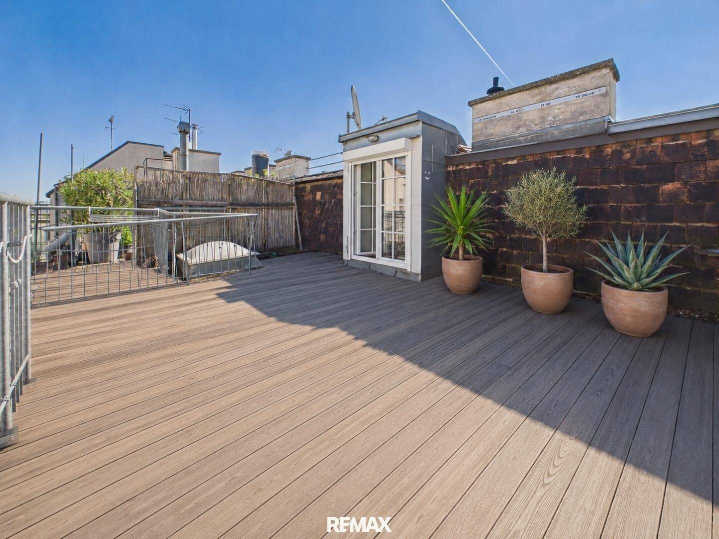 Geräumige Dachterrasse mit Holzdeck, Pflanzen und weitem Blick über die Dächer.