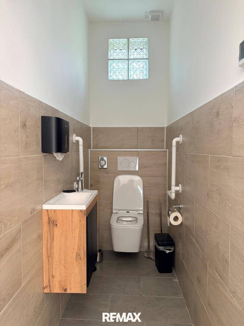 Modernes Gäste-WC mit Holzoptik-Fliesen, Wand-WC und kleinem Waschbecken, beleuchtet durch Glasbausteine.