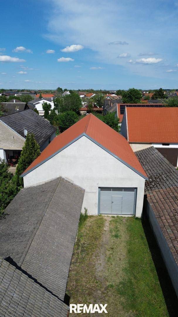 Luftaufnahme eines Gebäudes mit rotem Satteldach und Garagentor, umgeben von weiteren Häusern und Grünflächen.