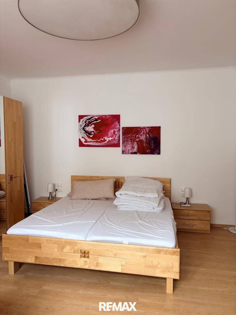 Helles Schlafzimmer mit Holzbett, Nachttischen und Laminatboden, dekoriert mit roten Kunstwerken an der Wand.