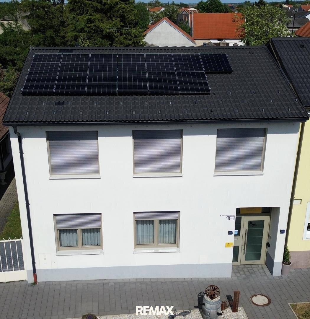 Luftaufnahme eines modernen Einfamilienhauses mit Photovoltaikanlage auf dem Dach und Rollläden an den Fenstern.