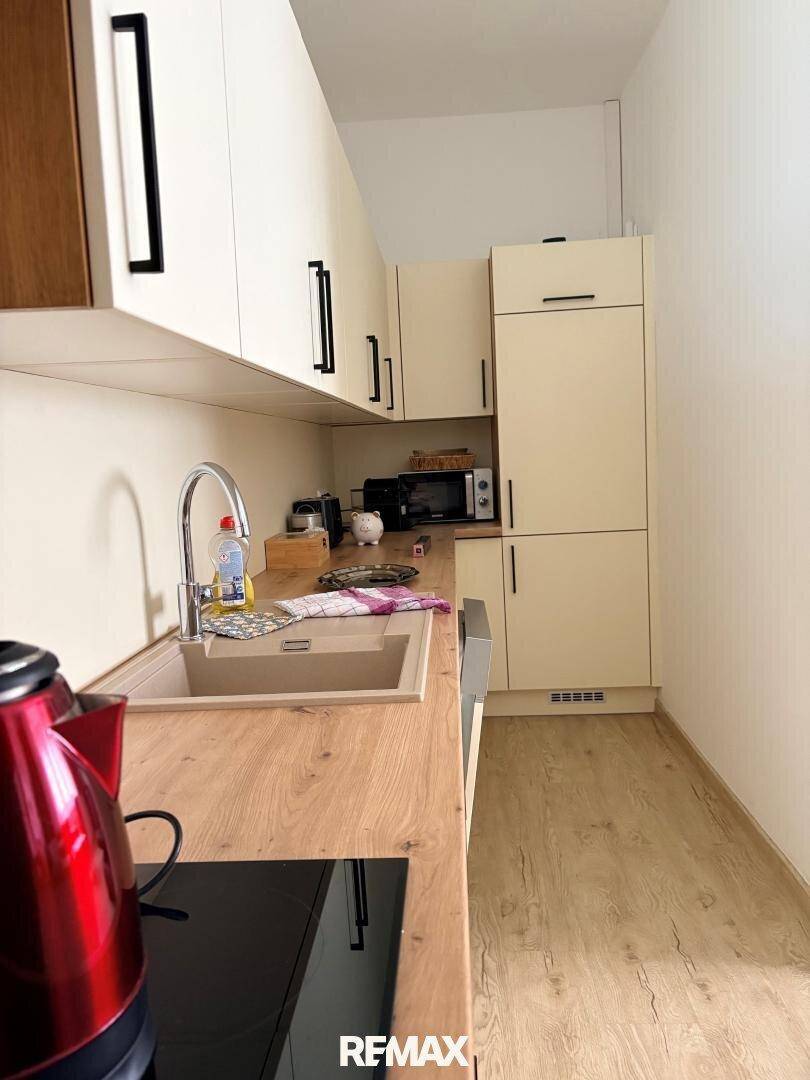 Schmale Küche mit beigen Schränken, Holzarbeitsplatte und Laminatboden, ausgestattet mit modernen Geräten.