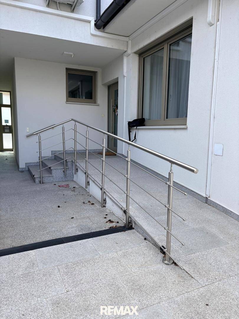 Eingangsbereich eines Hauses mit Rampe und Treppe, ausgestattet mit einem modernen Edelstahlgeländer für Barrierefreiheit.