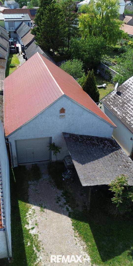 Luftaufnahme eines Gebäudes mit rotem Satteldach und Carport, umgeben von Bäumen und einer Zufahrt.