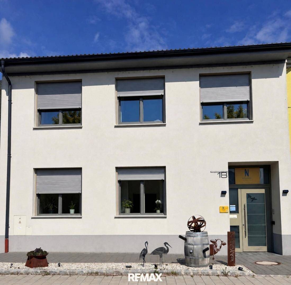Moderne Hausfassade mit großen Fenstern, Rollläden und einer gepflegten Vorgartengestaltung.