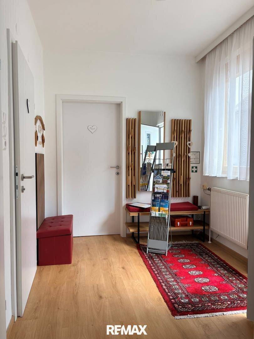 Freundlicher Flur mit Holzboden, Garderobe und einem roten Teppich, der zum Eingangsbereich führt.