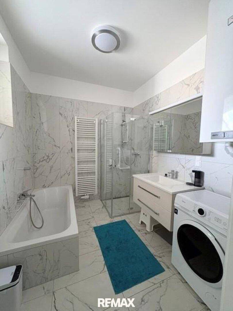 Modernes Badezimmer mit Badewanne, Duschkabine, Waschbecken und beheiztem Handtuchhalter, gefliest in Marmoroptik.