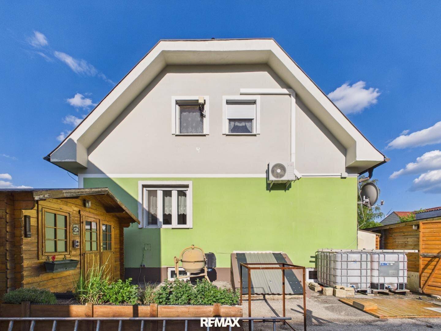 Seitenansicht des Hauses mit einem Gartenhaus, Klimaanlage und Wasserbehältern im Außenbereich.