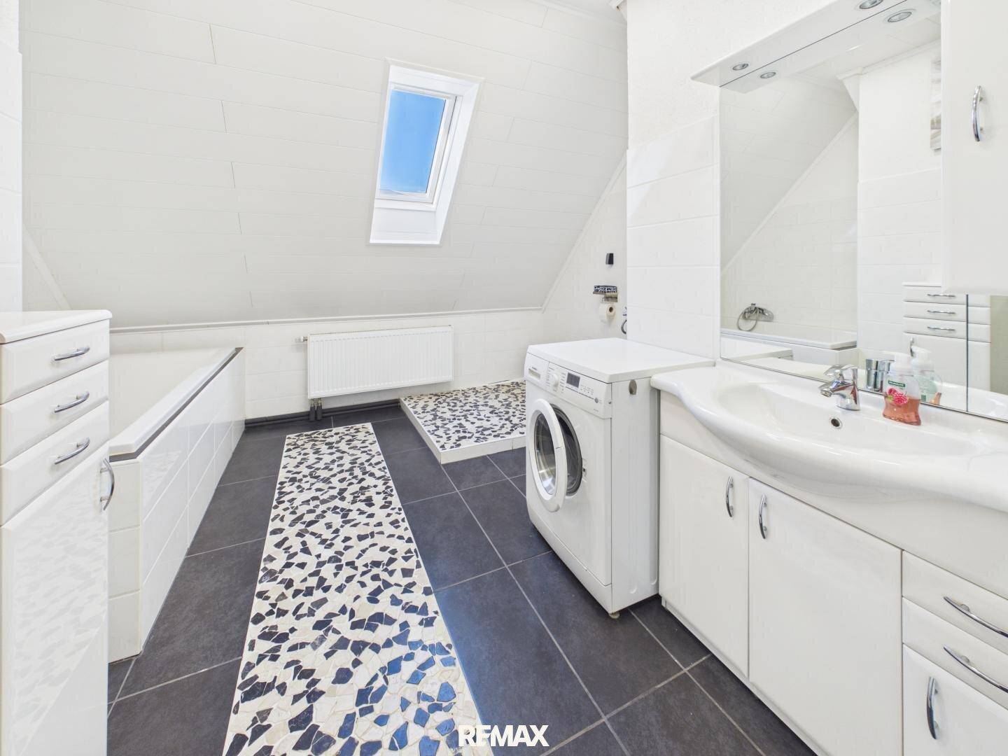 Dachgeschoss-Badezimmer mit Badewanne, Waschmaschine und Dachfenster für natürliches Licht.