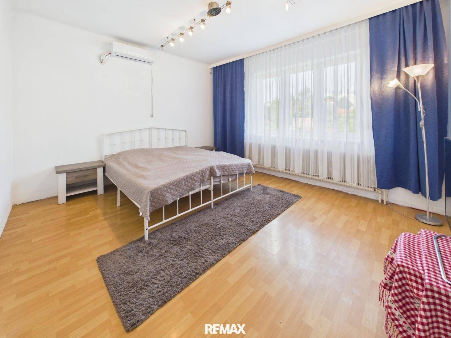 Schlafzimmer mit Holzboden, Doppelbett und blauen Vorhängen, ausgestattet mit einer Klimaanlage.