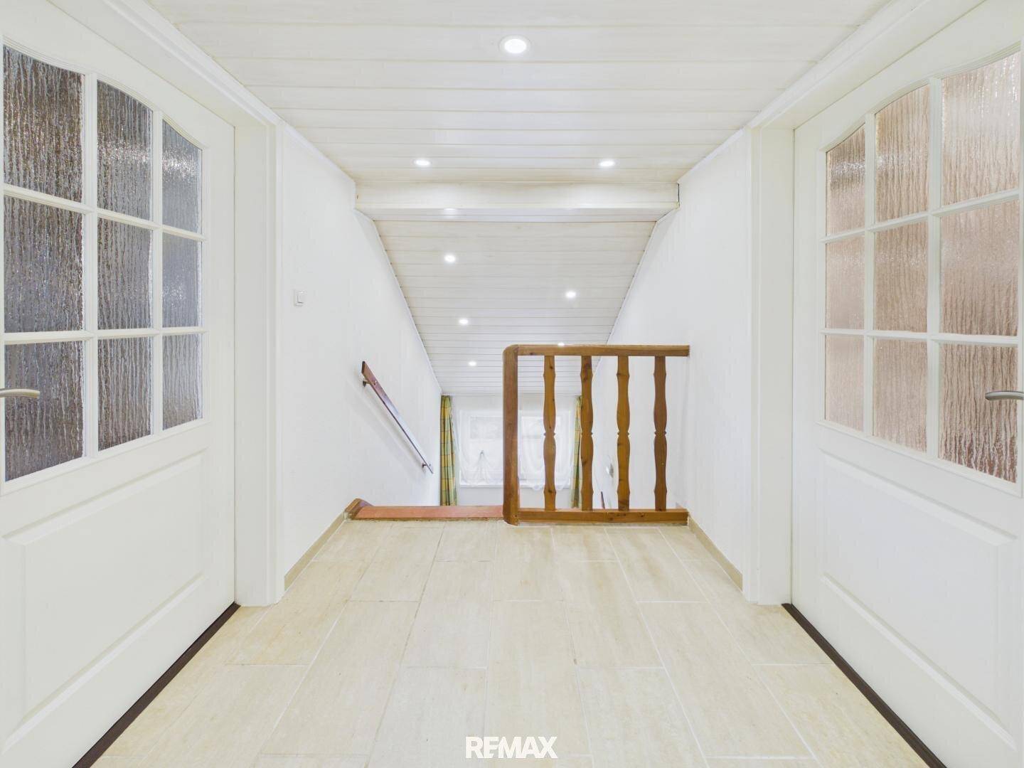 Oberer Flur mit Fliesenboden und Holzbalken an der Decke, der zu weiteren Zimmern führt.