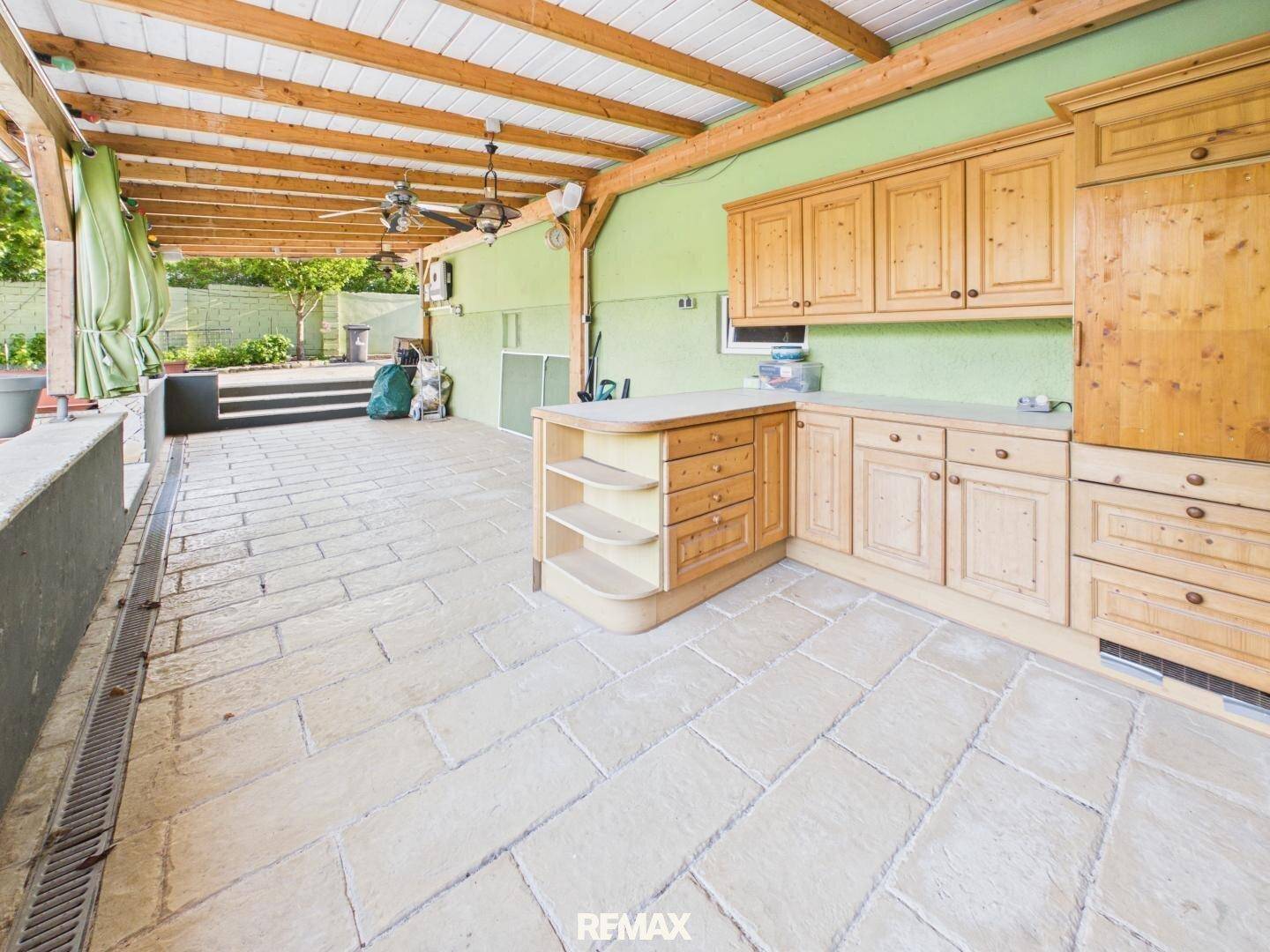 Überdachte Terrasse mit Außenküche, Fliesenboden und Blick in den grünen Gartenbereich.