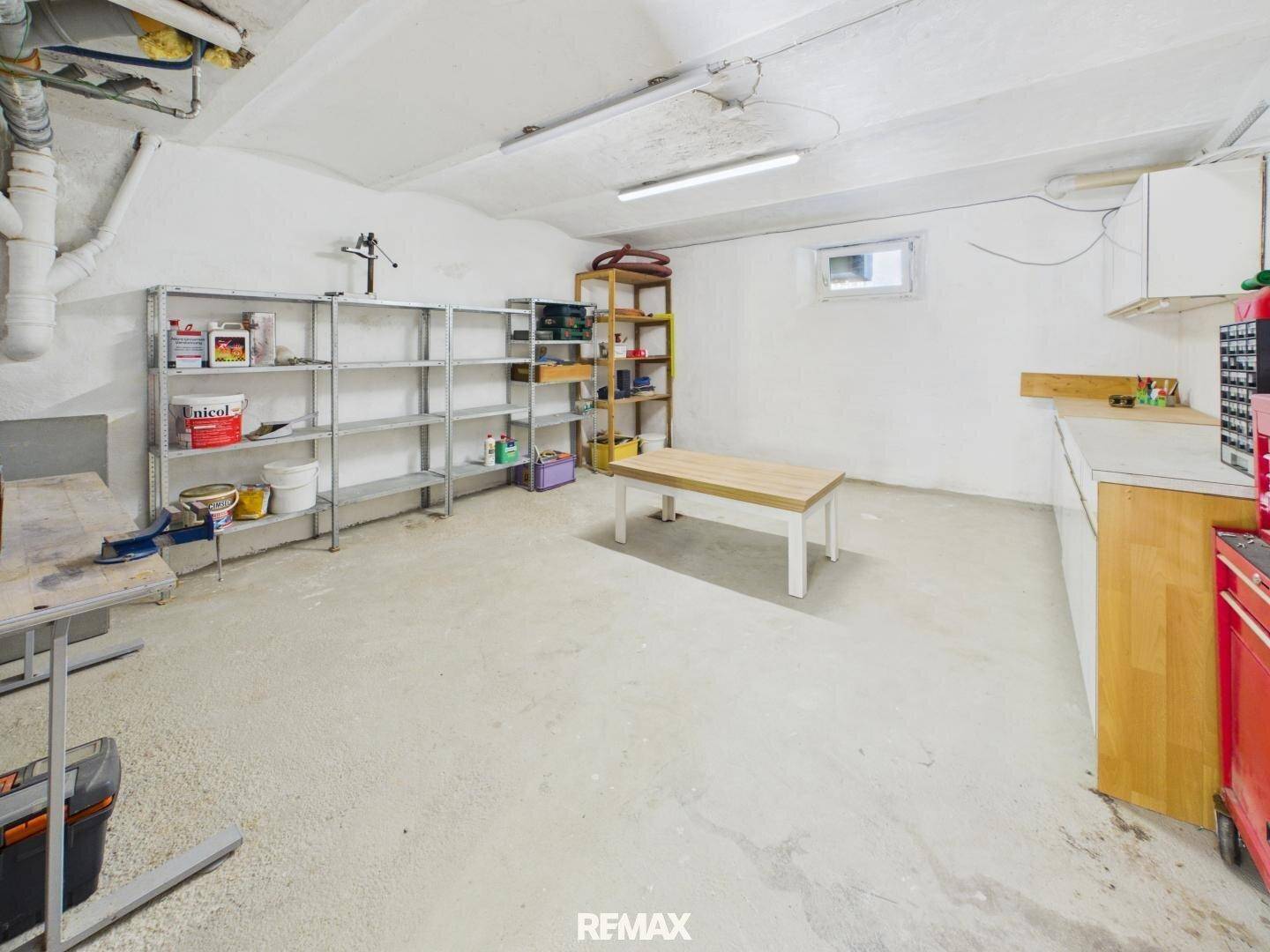 Großer Kellerraum mit Betonboden und Regalen, geeignet für Lagerung oder als Werkstatt.
