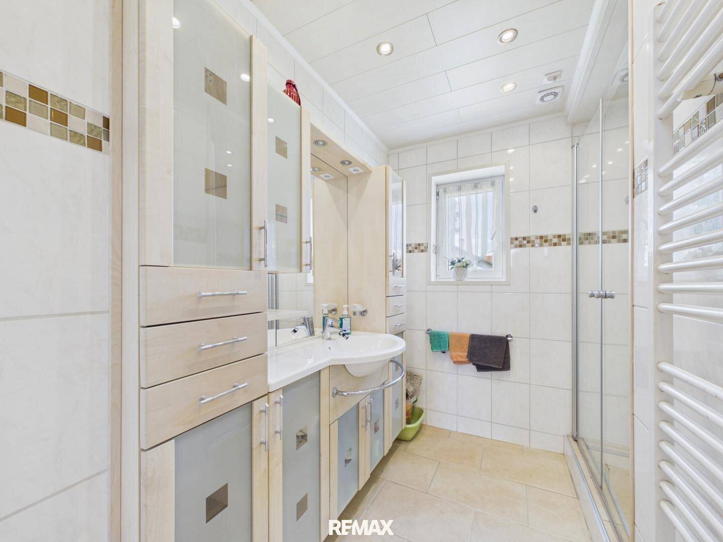 Modernes Badezimmer mit weißen Fliesen, Waschtischunterschrank, Duschkabine und Handtuchheizkörper.