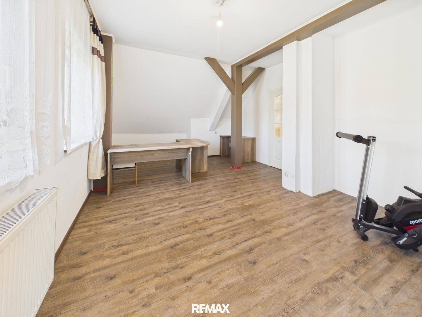 Dachgeschosszimmer mit Laminatboden, sichtbaren Holzbalken und einem Schreibtischbereich.
