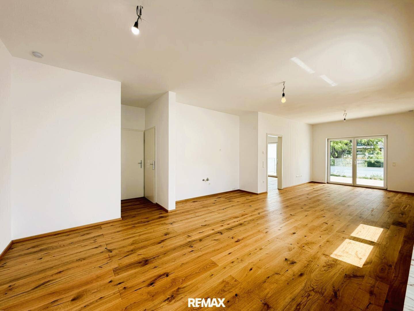 Heller, leerer Raum mit Holzboden und Zugang zu einem Außenbereich durch eine Glasschiebetür.