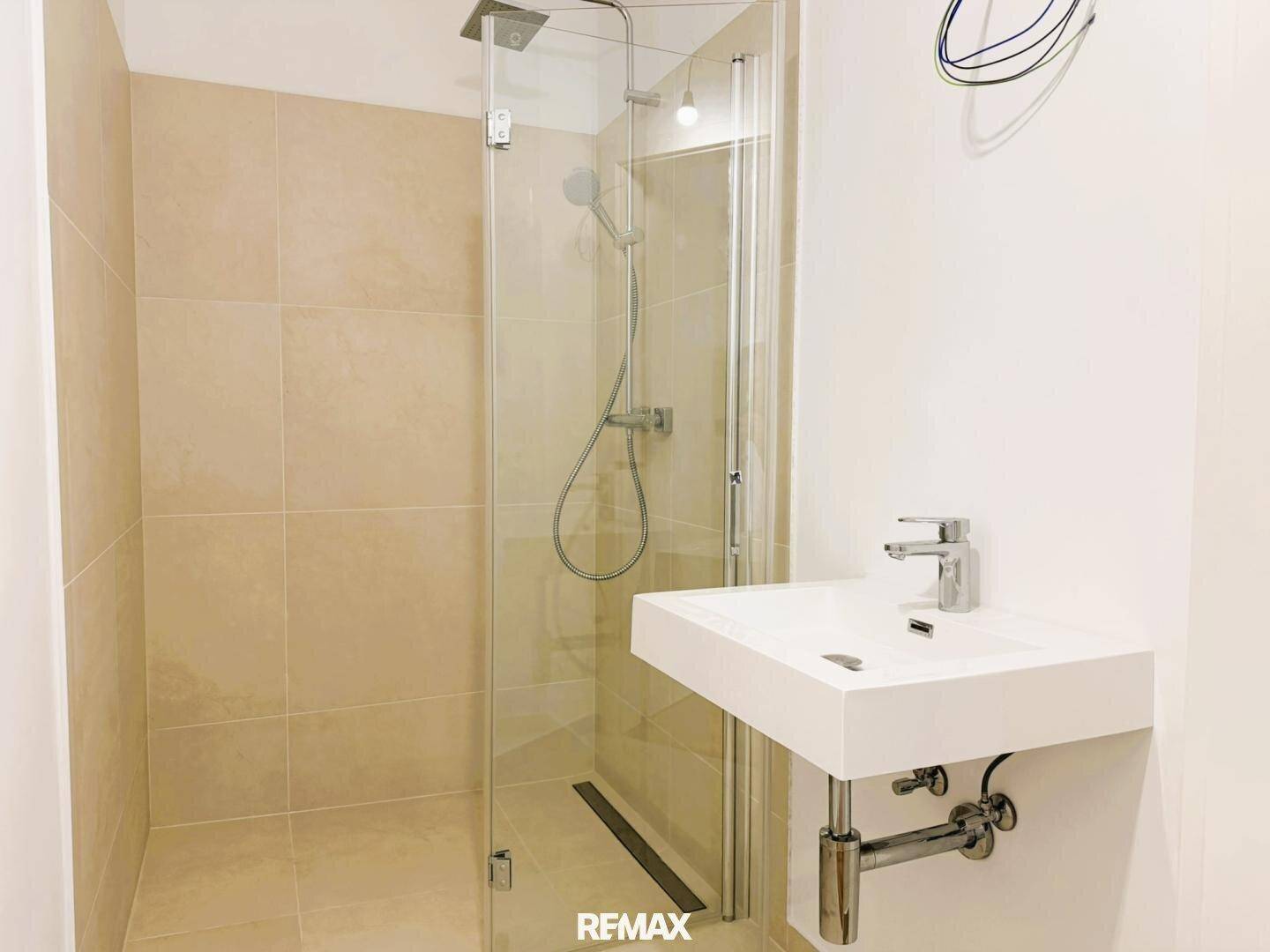 Modernes Badezimmer mit ebenerdiger Dusche, Einzelwaschbecken und hellen Fliesen an Wänden und Boden.