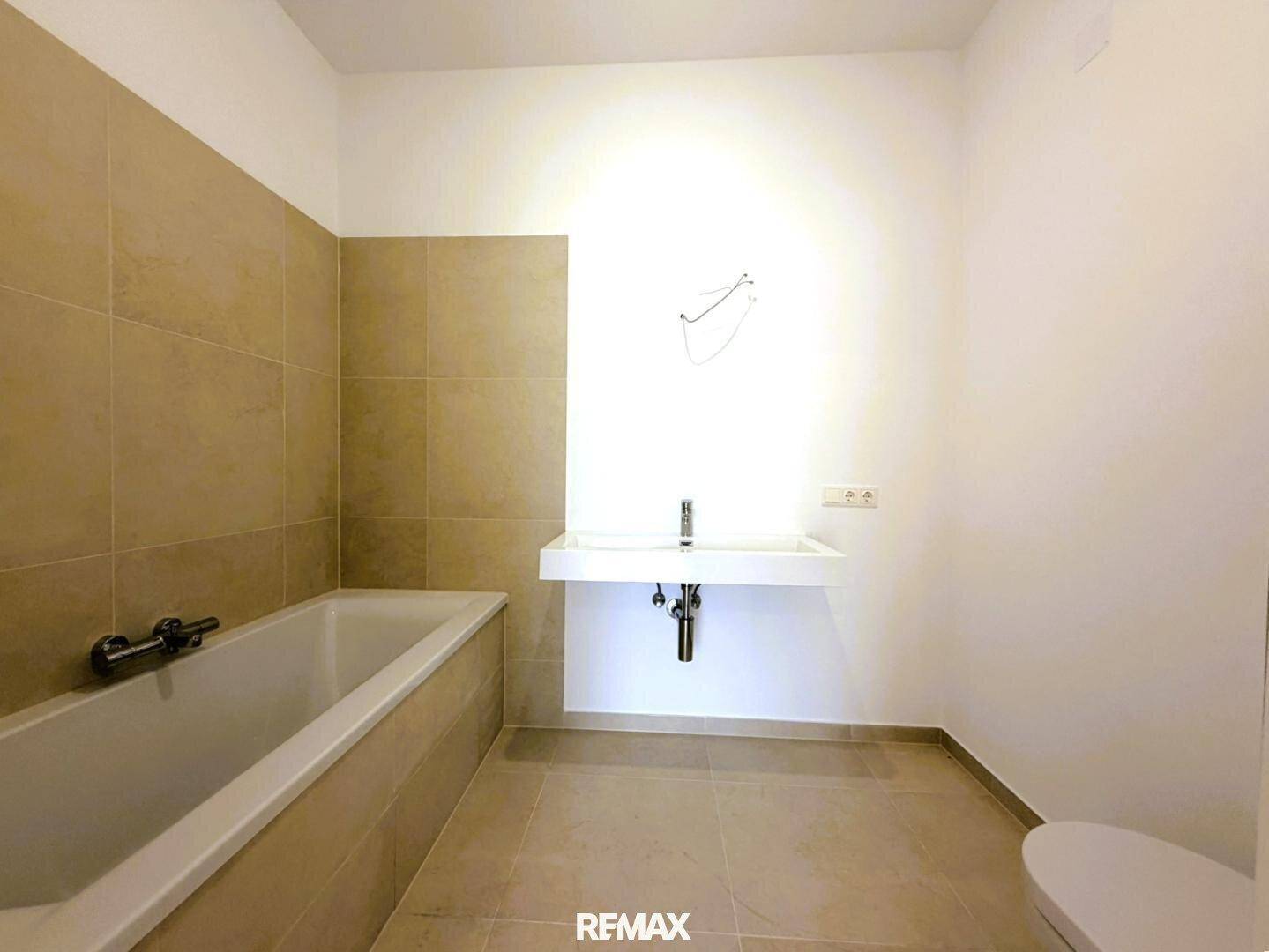 Modernes Badezimmer mit Badewanne, Einzelwaschbecken und hellen Fliesen an Wänden und Boden.