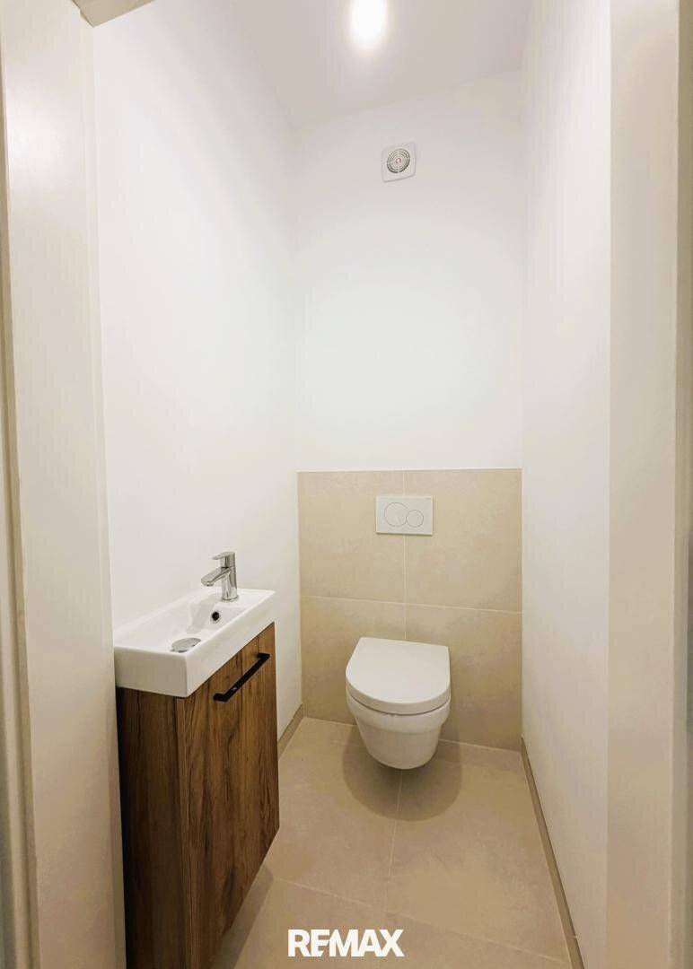 Kleines Gäste-WC mit wandhängender Toilette, kleinem Waschbecken und hellen Fliesen.