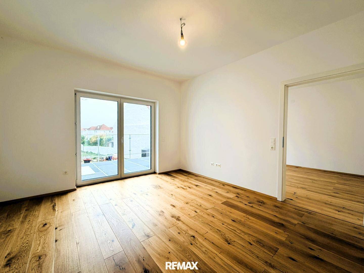 Heller Raum mit Holzboden und großer Glasschiebetür, die viel Licht und Zugang nach draußen ermöglicht.