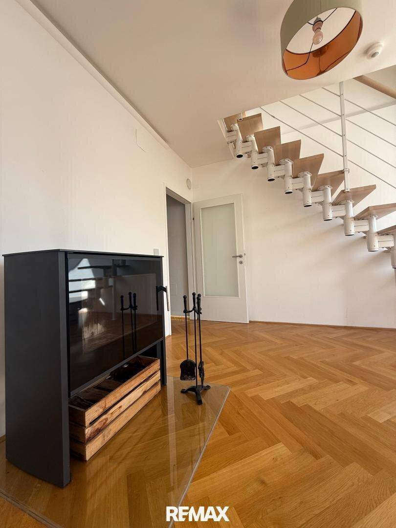 Heller Wohnbereich mit Fischgrätparkett, modernem Kaminofen und offener Treppe zum Obergeschoss.
