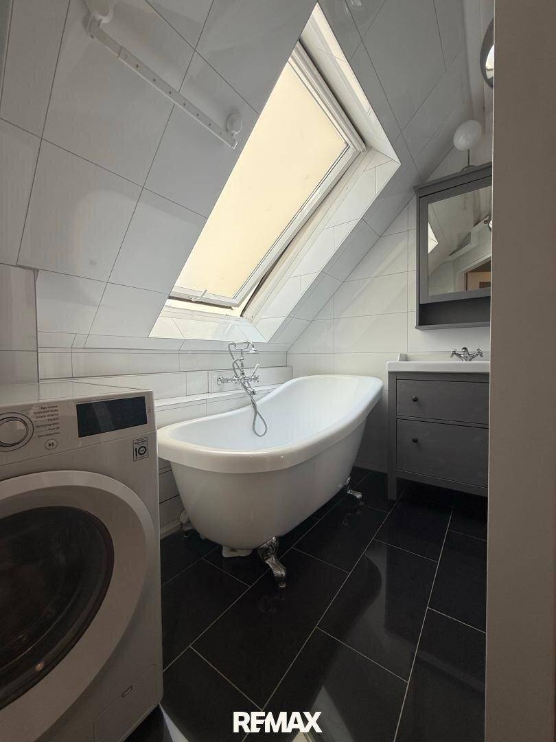 Modernes Badezimmer im Dachgeschoss mit freistehender Badewanne, Dachfenster und Waschmaschine.