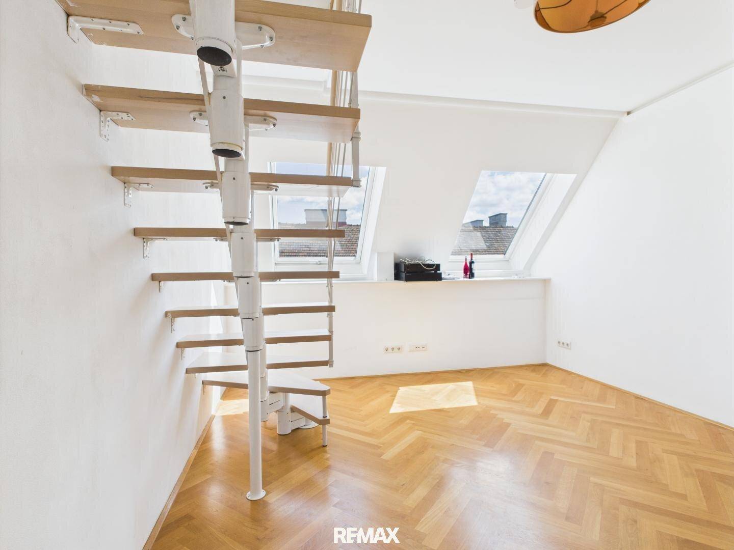 Offener Raum mit Wendeltreppe, Fischgrätparkett und Dachfenstern, bietet viel Tageslicht.