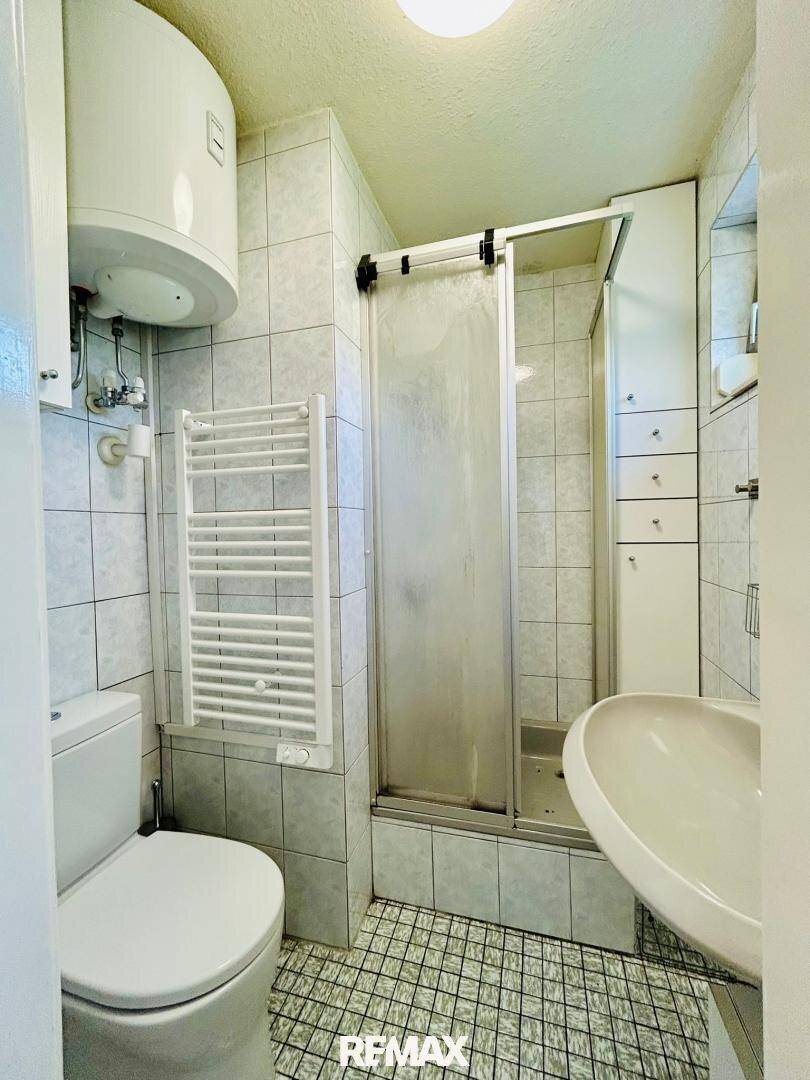 Kleines Badezimmer mit Dusche, WC, Waschbecken und Handtuchheizkörper.