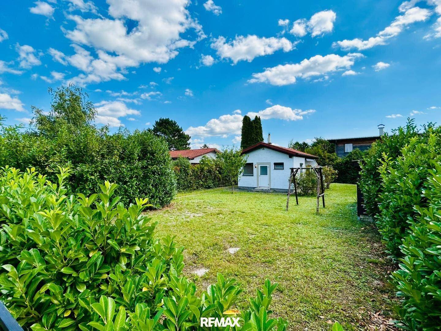 Großer, gepflegter Garten mit Rasenfläche, Hecken und einem Schaukelgestell im Hintergrund.