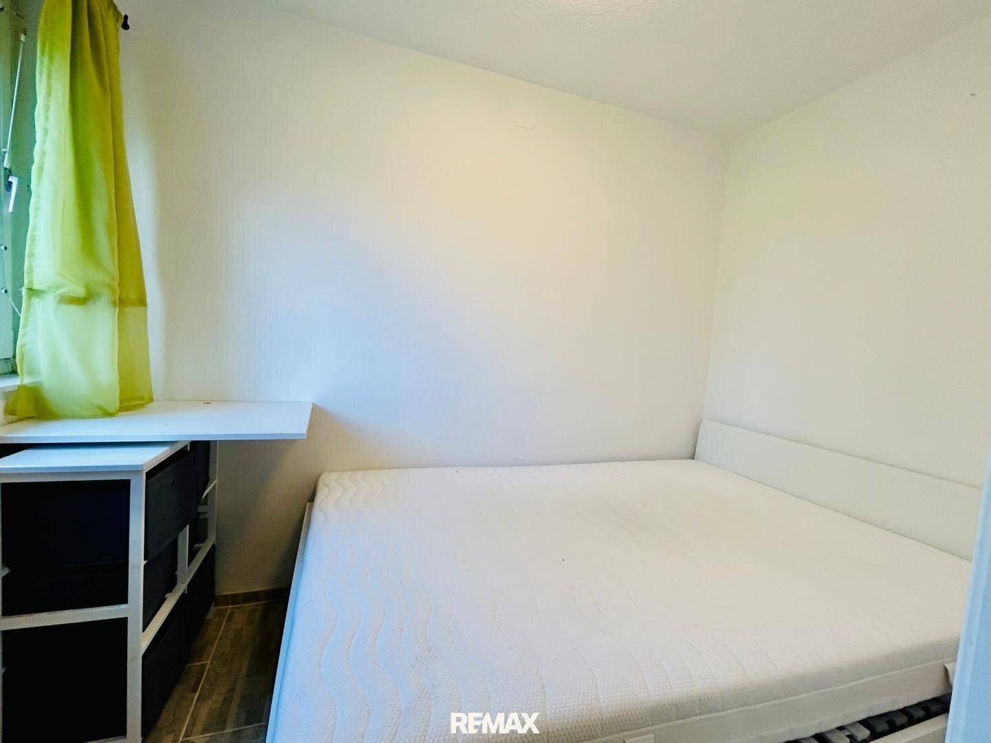 Helles Schlafzimmer mit Doppelbett, schlichten Möbeln und Fenster mit Vorhang.