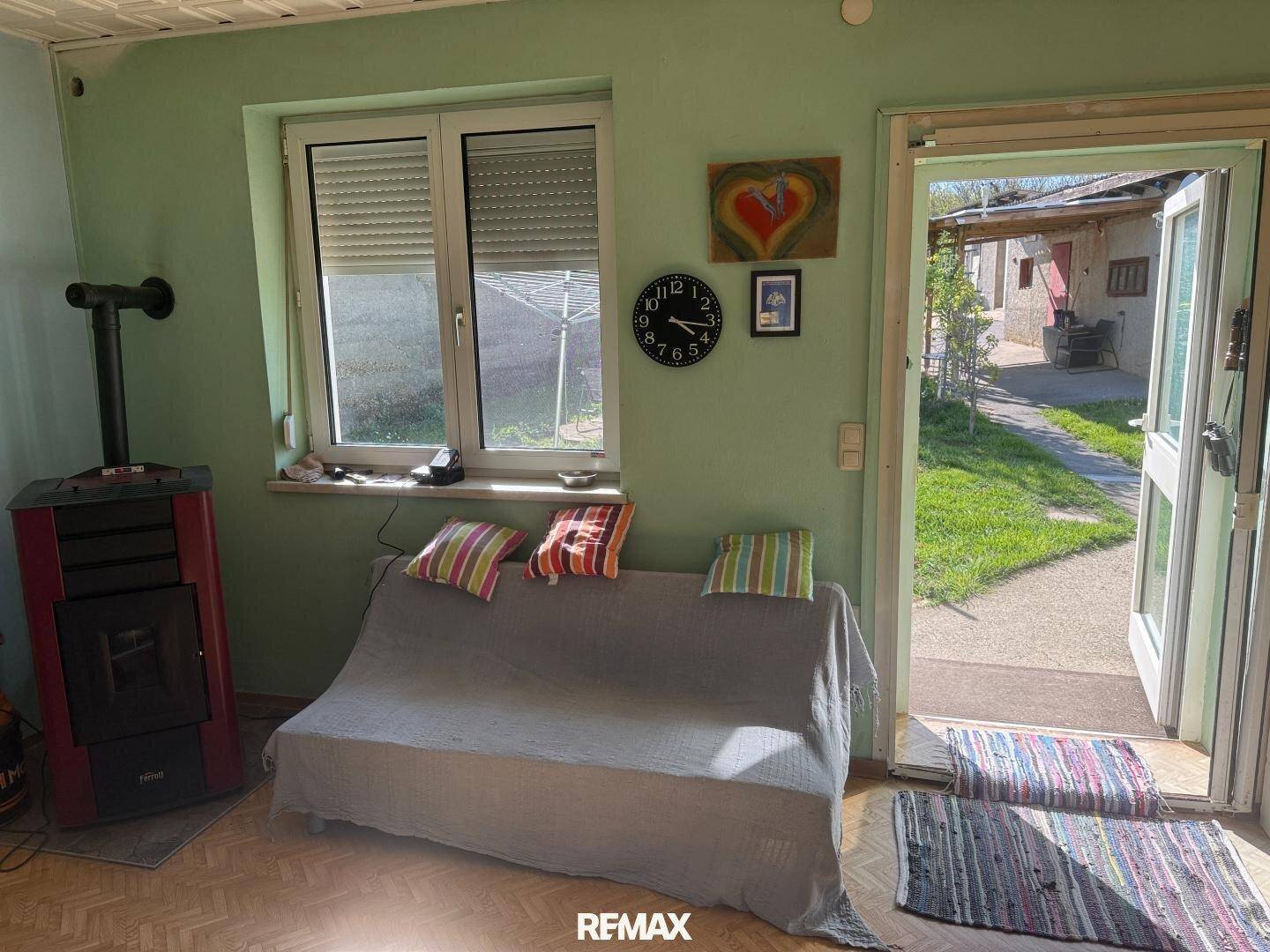 Gemütliches Wohnzimmer mit Kaminofen, Sofa und Zugang zum Garten, hell und einladend.